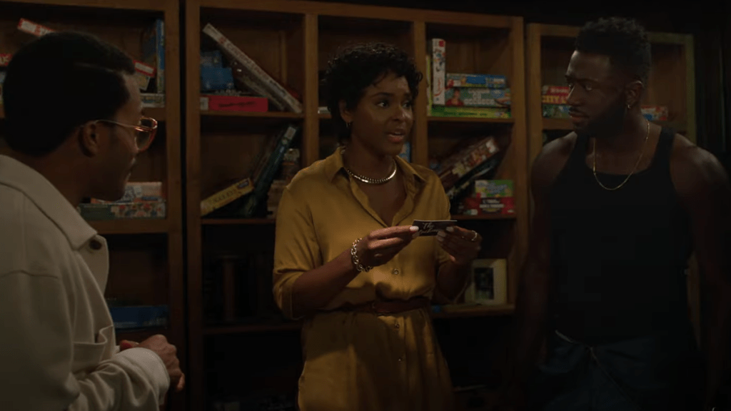 A Black woman in a yellow shirt reads from a game card while her two male friends, also Black, stand listening.