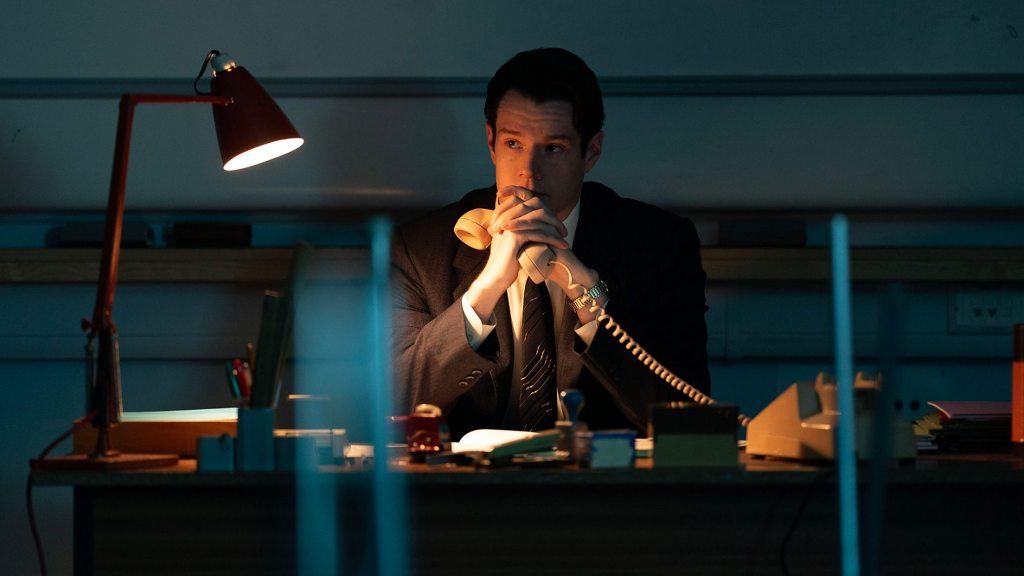 A man sits while holding a phone in his hand.