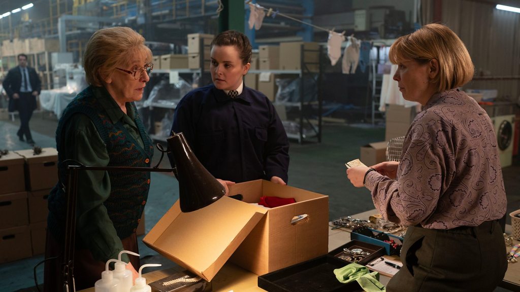 Three women stand in front of a box.