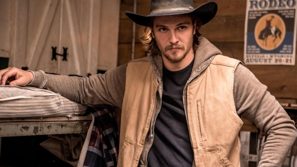 Luke Grimes leans up against a bed.