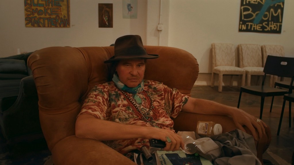 Val Kilmer sits on a seat.