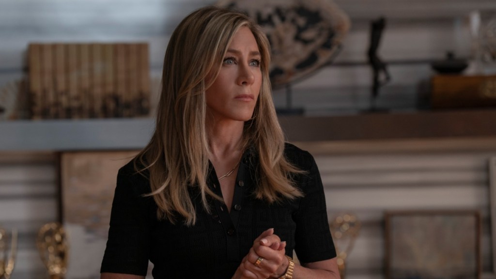 Jennifer Aniston stands with hands clasped.