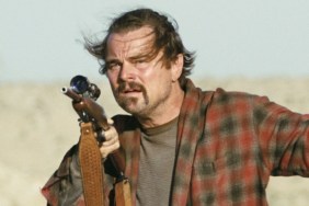 Leonardo DiCaprio holds a gun and points it.