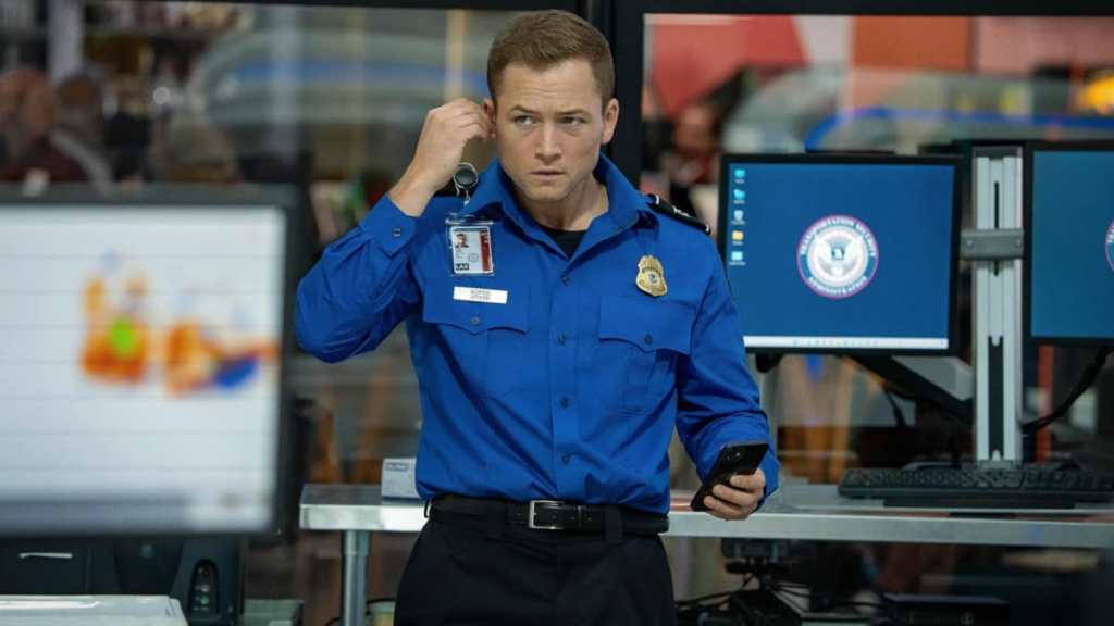 Taron Egerton puts an ear piece on in Carry-On.